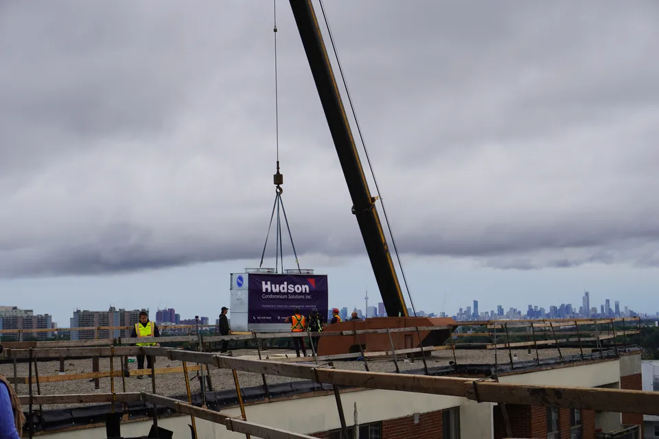Crane positioning the new cooling tower on the condominium roof